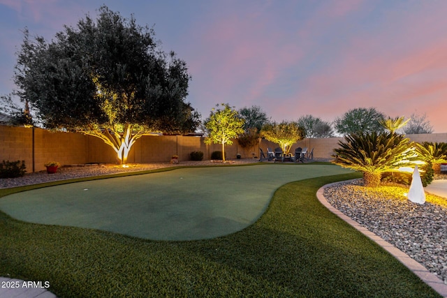 yard at dusk featuring an area to practice putting and a fenced backyard