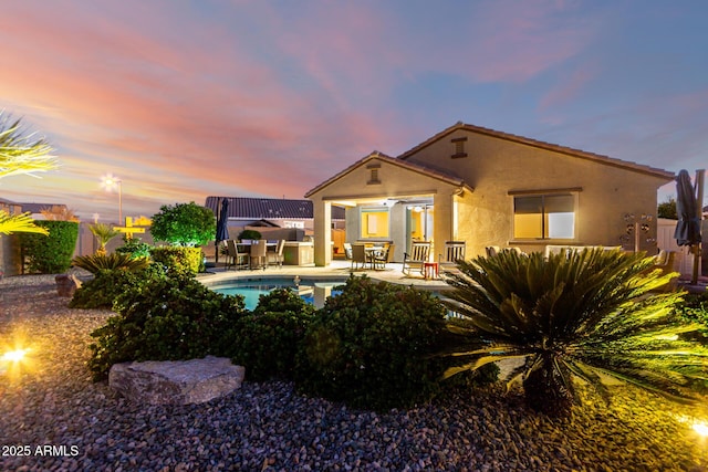 rear view of property featuring stucco siding, a patio area, an outdoor pool, and fence