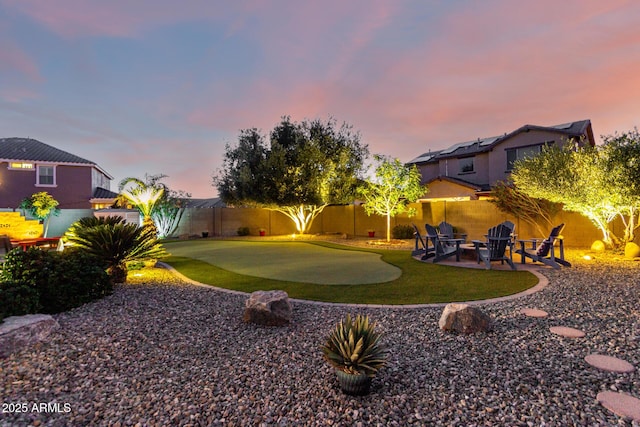 yard at dusk with a putting area, a fenced backyard, and a patio