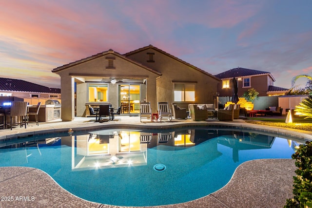 pool at dusk featuring an outdoor living space, a patio, an outdoor pool, and exterior kitchen