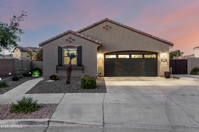 mediterranean / spanish home with stucco siding, a garage, fence, and driveway