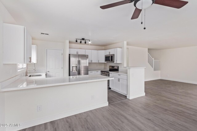 kitchen featuring appliances with stainless steel finishes, hardwood / wood-style floors, sink, white cabinets, and kitchen peninsula