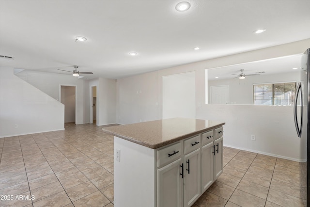 kitchen with ceiling fan, light tile patterned floors, white cabinets, a center island, and stainless steel refrigerator