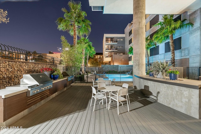 deck at dusk with an outdoor kitchen, area for grilling, and a community pool