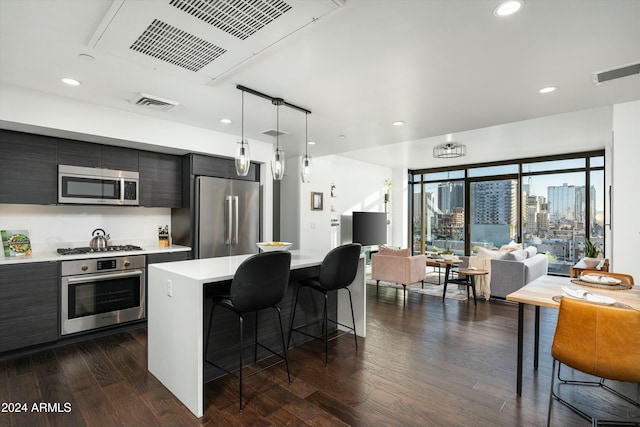 kitchen featuring dark hardwood / wood-style floors, pendant lighting, a kitchen bar, a kitchen island, and appliances with stainless steel finishes