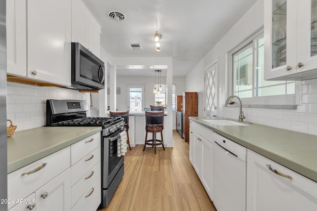 kitchen featuring pendant lighting, sink, light wood-type flooring, appliances with stainless steel finishes, and white cabinetry