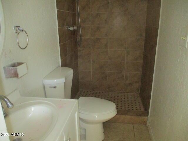 full bathroom with toilet, tile patterned flooring, tiled shower, and vanity