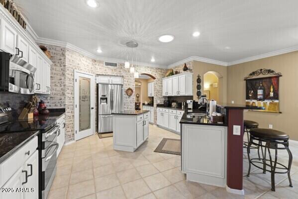 kitchen with sink, appliances with stainless steel finishes, a kitchen island, pendant lighting, and white cabinets