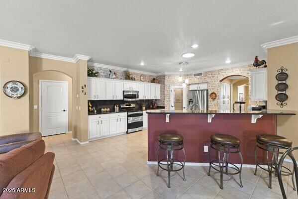 kitchen featuring white cabinetry, appliances with stainless steel finishes, a breakfast bar, and crown molding