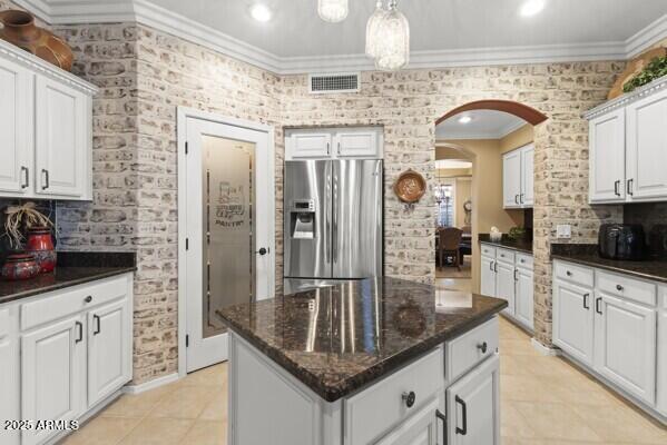 kitchen with stainless steel fridge, dark stone countertops, ornamental molding, white cabinets, and a kitchen island