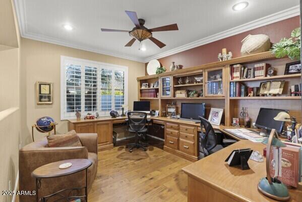 office area with crown molding, built in desk, ceiling fan, and light wood-type flooring