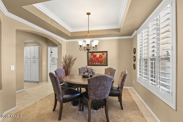 dining room with light tile patterned flooring, a notable chandelier, crown molding, and a tray ceiling