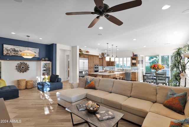 living room featuring ceiling fan, light wood-type flooring, and sink