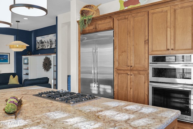 kitchen with light stone counters, hanging light fixtures, and appliances with stainless steel finishes