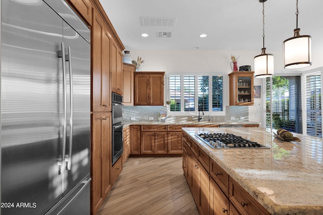 kitchen featuring backsplash, light stone counters, stainless steel appliances, sink, and decorative light fixtures