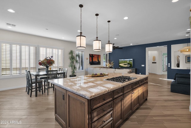 kitchen with light stone countertops, light hardwood / wood-style floors, decorative light fixtures, stainless steel gas stovetop, and a kitchen island