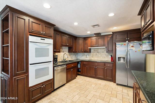 kitchen with decorative backsplash, appliances with stainless steel finishes, dark stone counters, a textured ceiling, and sink