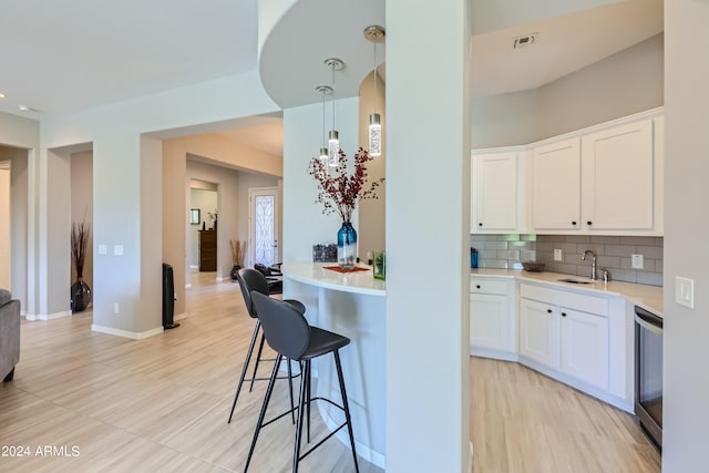 kitchen featuring a breakfast bar area, sink, pendant lighting, white cabinets, and tasteful backsplash