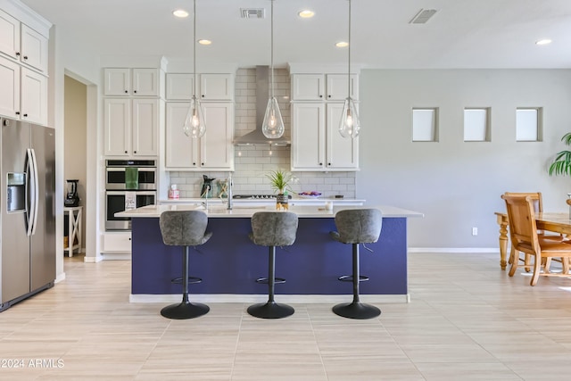 kitchen with appliances with stainless steel finishes, wall chimney exhaust hood, white cabinets, and a center island with sink