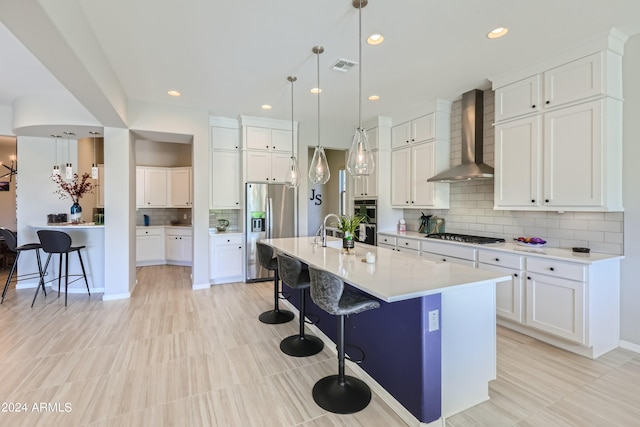 kitchen featuring white cabinetry, stainless steel appliances, wall chimney exhaust hood, a breakfast bar area, and a kitchen island with sink