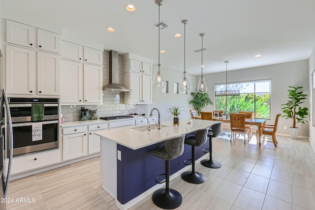 kitchen with wall chimney exhaust hood, white cabinetry, and a kitchen island with sink