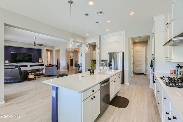 kitchen with white cabinets, a center island with sink, ceiling fan, stainless steel appliances, and decorative light fixtures