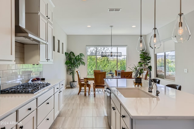 kitchen with sink, white cabinetry, stainless steel appliances, wall chimney exhaust hood, and a center island with sink