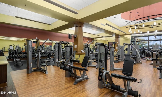 exercise room with decorative columns, wood-type flooring, and a chandelier