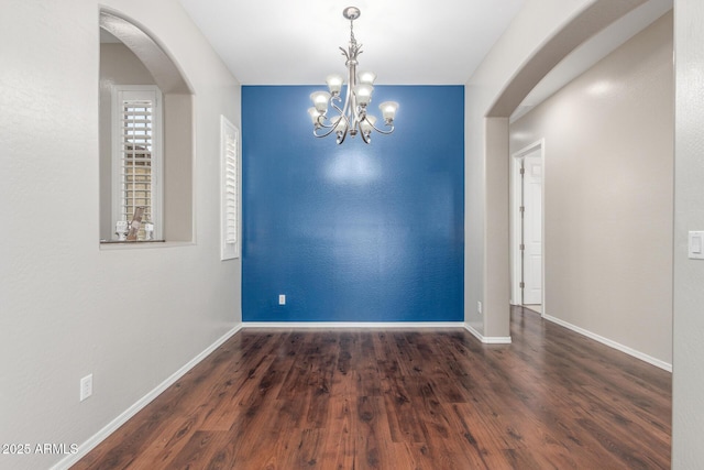empty room featuring baseboards, arched walkways, a chandelier, and wood finished floors