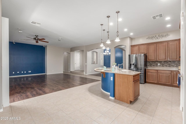 kitchen featuring open floor plan, a ceiling fan, stainless steel refrigerator with ice dispenser, visible vents, and arched walkways