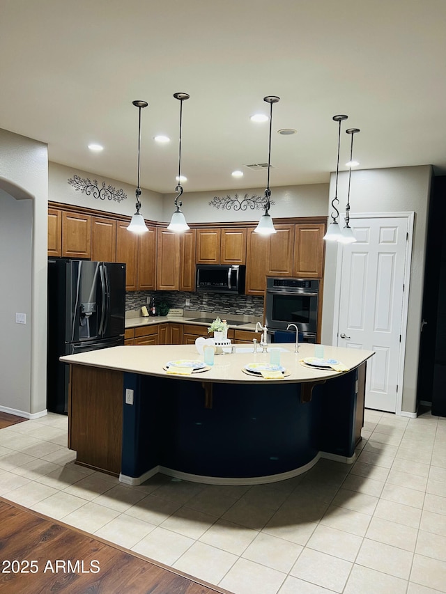 kitchen featuring light tile patterned floors, black appliances, light countertops, decorative backsplash, and a spacious island
