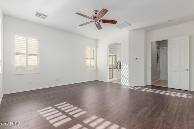 empty room with arched walkways, ceiling fan, visible vents, and dark wood-style flooring