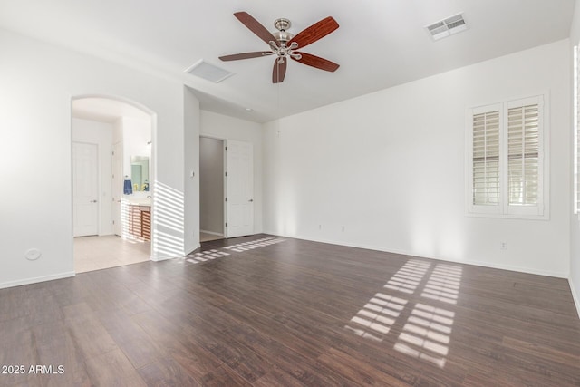 empty room with ceiling fan, arched walkways, visible vents, wood finished floors, and baseboards