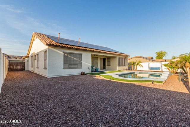 back of house featuring roof mounted solar panels, a fenced backyard, a tile roof, a patio, and stucco siding