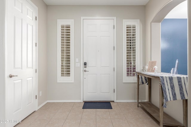 foyer entrance with arched walkways, light tile patterned flooring, and baseboards