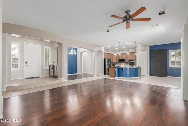 unfurnished living room featuring arched walkways, ceiling fan with notable chandelier, light tile patterned flooring, and visible vents