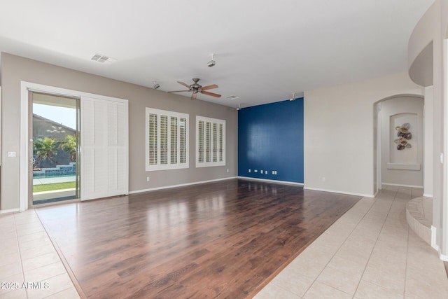unfurnished living room with visible vents, baseboards, arched walkways, a ceiling fan, and wood finished floors