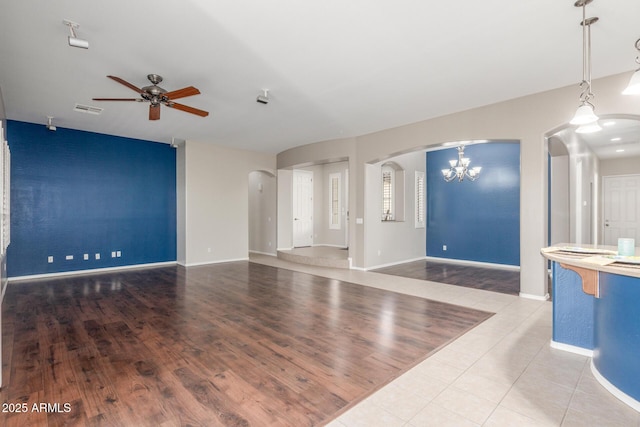 unfurnished living room with ceiling fan with notable chandelier, arched walkways, tile patterned flooring, visible vents, and baseboards