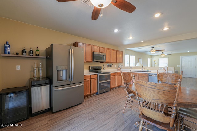 kitchen with sink, ceiling fan, light hardwood / wood-style floors, kitchen peninsula, and stainless steel appliances