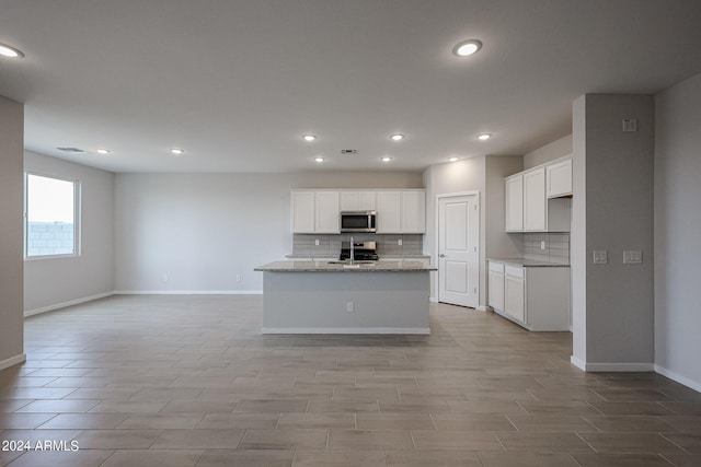 kitchen with sink, stainless steel appliances, white cabinets, light stone counters, and a center island with sink