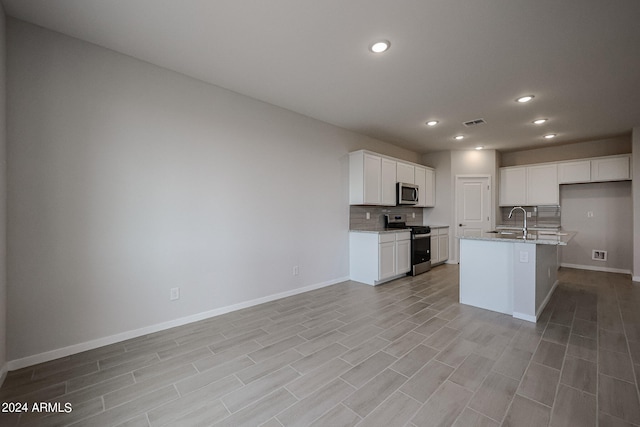 kitchen with sink, stainless steel appliances, white cabinets, light stone counters, and a kitchen island with sink