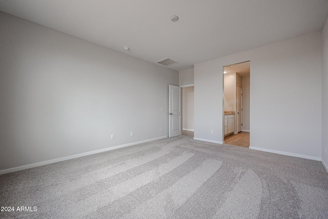 unfurnished bedroom with ensuite bathroom and light colored carpet