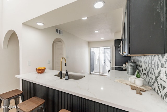 kitchen featuring visible vents, light stone countertops, a kitchen bar, a peninsula, and a sink