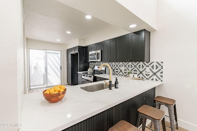 kitchen with a sink, light stone counters, a kitchen breakfast bar, backsplash, and stainless steel appliances