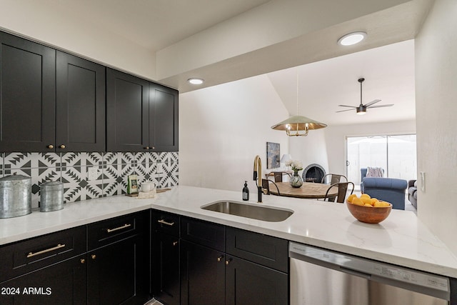 kitchen featuring tasteful backsplash, dark cabinets, a peninsula, stainless steel dishwasher, and a sink