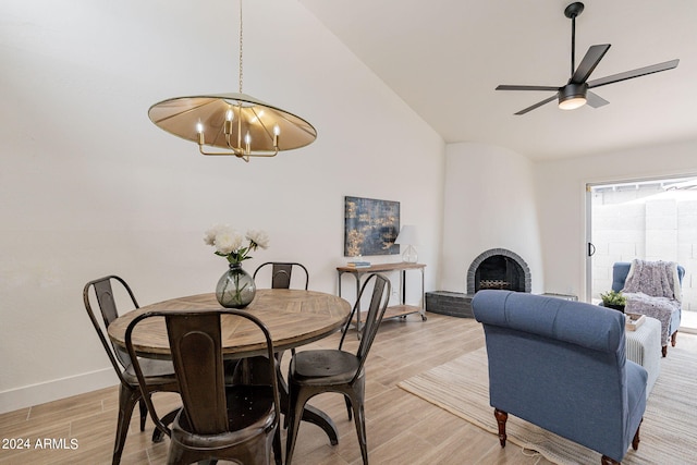 dining area with baseboards, lofted ceiling, light wood-style flooring, a fireplace, and ceiling fan with notable chandelier