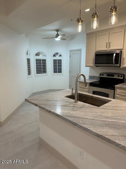 kitchen featuring hanging light fixtures, light stone countertops, appliances with stainless steel finishes, and a sink