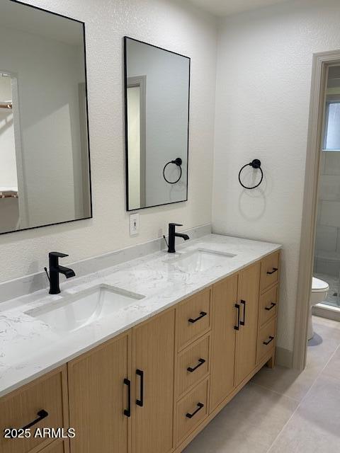 full bath with double vanity, tile patterned flooring, toilet, and a sink