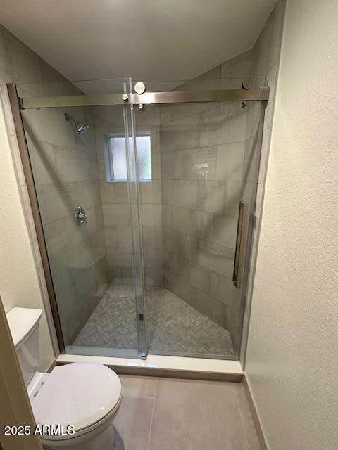 bathroom with a textured wall, a shower stall, and toilet