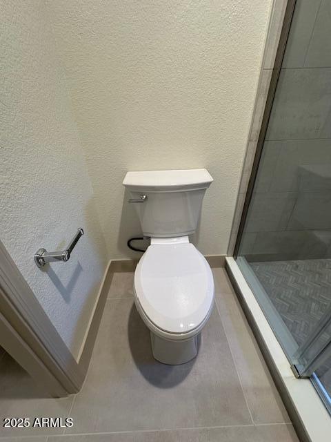 bathroom with a textured wall, a stall shower, toilet, and baseboards